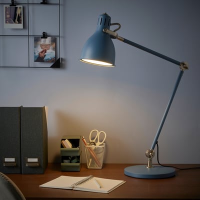 ARÖD blue desk lamp on wooden workspace, illuminating notebook and office supplies, with adjustable arms.