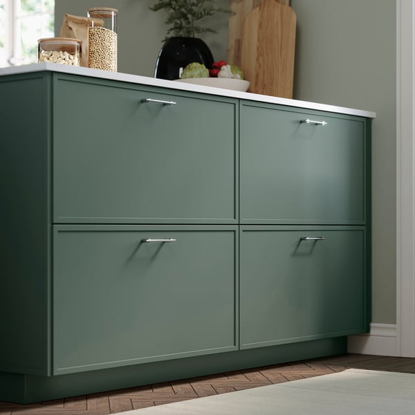 Dark grey-green kitchen cabinet, 4 silver-handled drawers, light green wall, white countertops, modern & functional.
