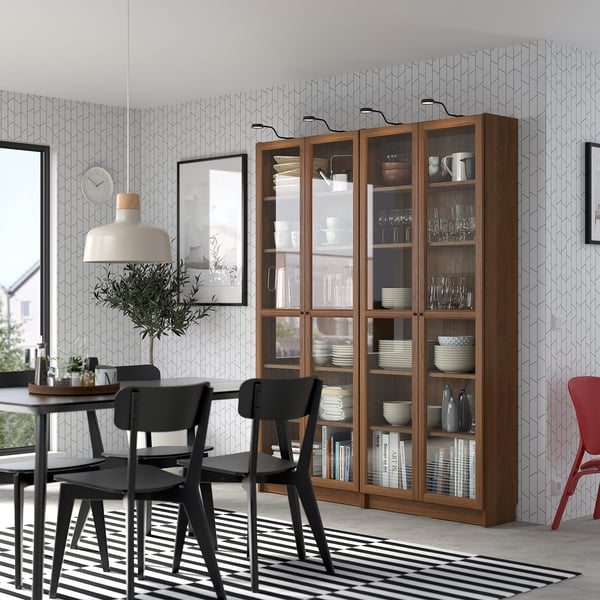 Modern dining area with BILLY bookcase, plates, and chairs. Striped rug, plant, and pendant lamp.