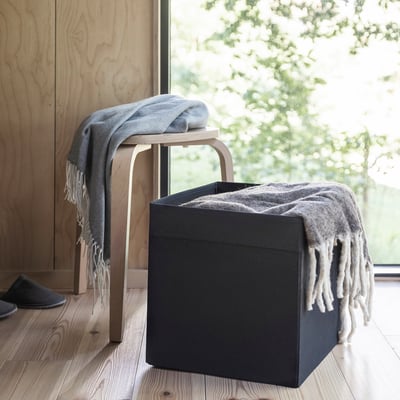 Black DRÖNA storage box with fringe, chair, greenery, slipper.