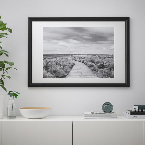 Framed photo on wall with white sideboard below, displaying home decor with picture, bowl, books, vase, and plant.