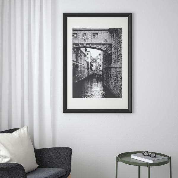 EDSBRUK frame on wall, displaying black-and-white bridge photo, next to sofa and side table with book.