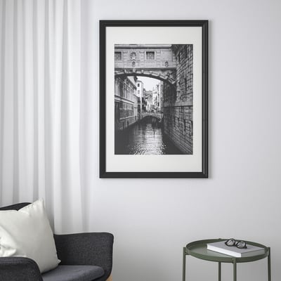 EDSBRUK frame on wall, displaying black-and-white bridge photo, next to sofa and side table with book.