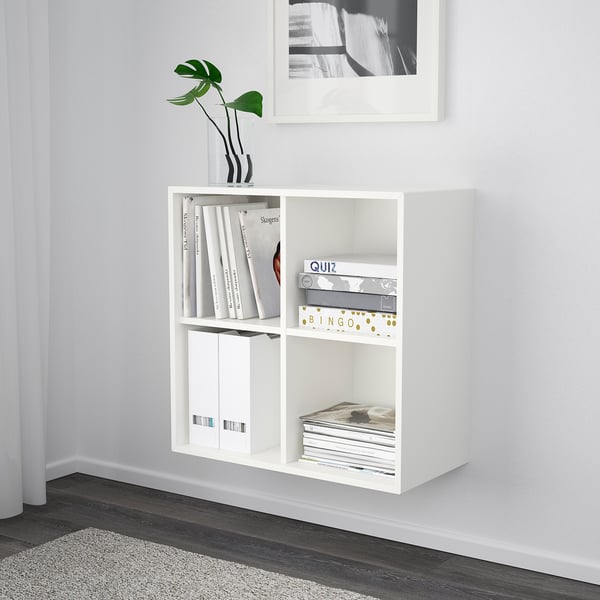 A white wall-mounted cabinet named EKET, holding books and games, with a plant on top and a black and white photo above.
