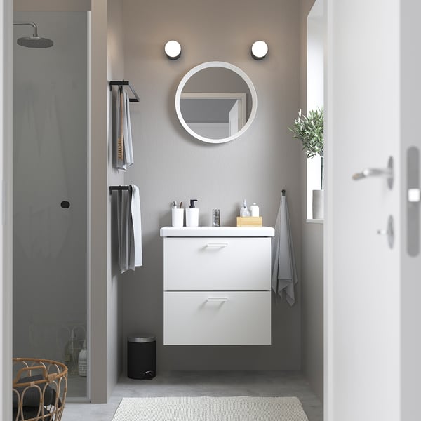 Modern white ENHET bathroom vanity with two drawers, mounted on wall, smaller than shower stall, with round mirror and lights above.