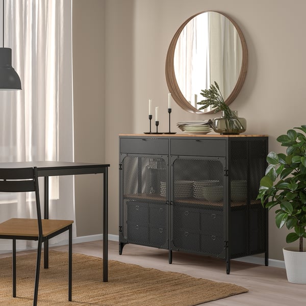 FJÄLLBO sideboard: black metal, wood top, three doors, cubic shape, rustic-industrial design, fits well in dining room, near table & plant.