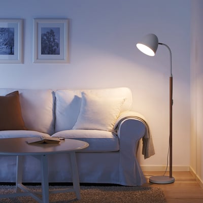 Cosy living room with white FRANSALG lamp, tall & slim, lighting a blue couch, beside a low table.