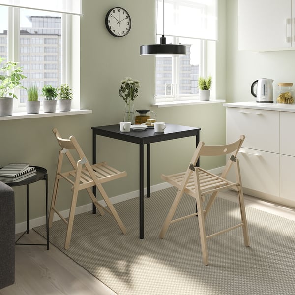 Dining setting with 2 black chairs, table, and flowers.