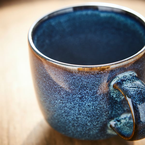 Beautiful blue glazed mug on table, shows texture and craftsmanship. Golden-rimmed handle.