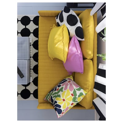 Bright yellow sofa with colourful pillows: floral, pink, yellow, cow print. Black and white patterned rug.