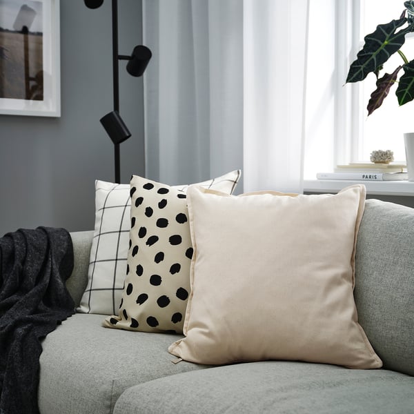 Modern sofa with GURLI pillows, one beige, one white with black spots, near window.