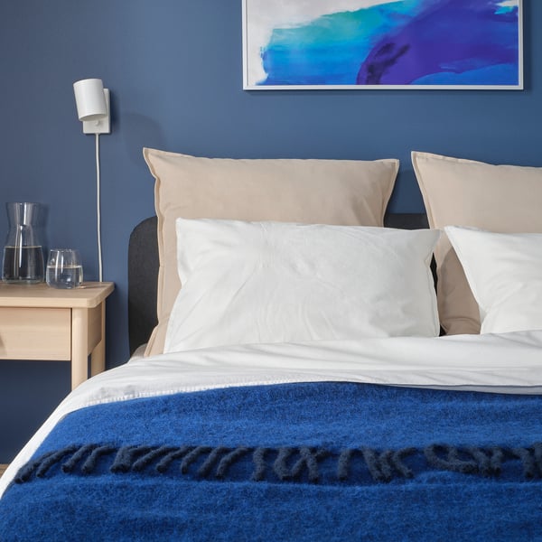 Bed with blue GURLI throw, white pillows, wall sconce, abstract art.