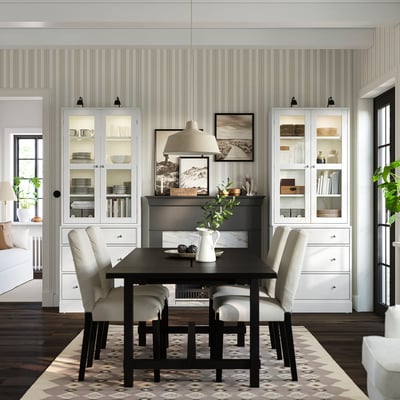 Modern dining room with black HAVSTA table, cream chairs, patterned rug, glass cabinets, striped walls, fireplace.