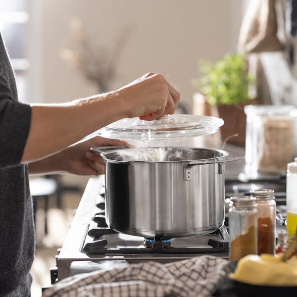 A person cooks on a gas stove with non-stick ceramic pots and a strainer.