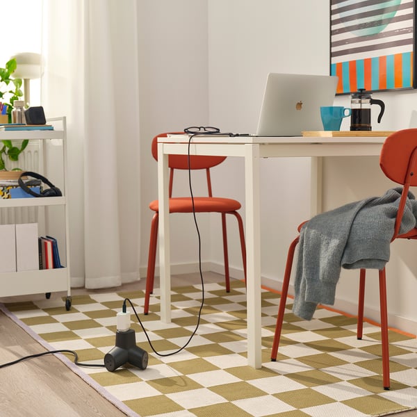 Home office scene: white desk, red chair, laptop, coffee cup, extension cord under desk.