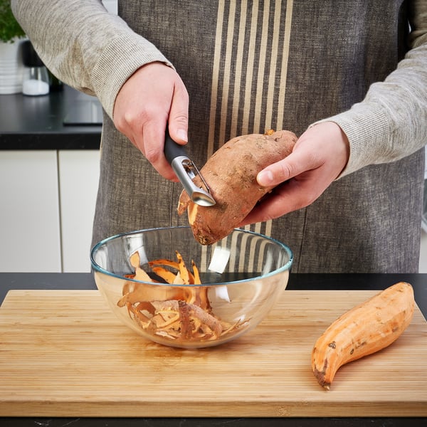 Person peels vegetable with IKEA peeler into bowl.