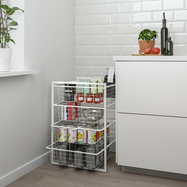 White JONAXEL storage rack, with various baskets, sitting between kitchen cabinets, holding small food items.