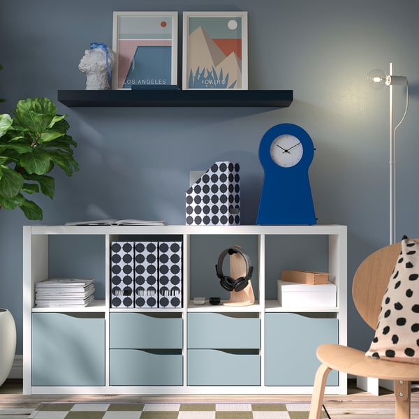 Home office with KALLAX shelf, blue clock, vases, books, chair.