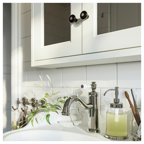 Modern bathroom with chrome tap, glass soap dispenser, toothbrush holder, green plant, and white cabinets.