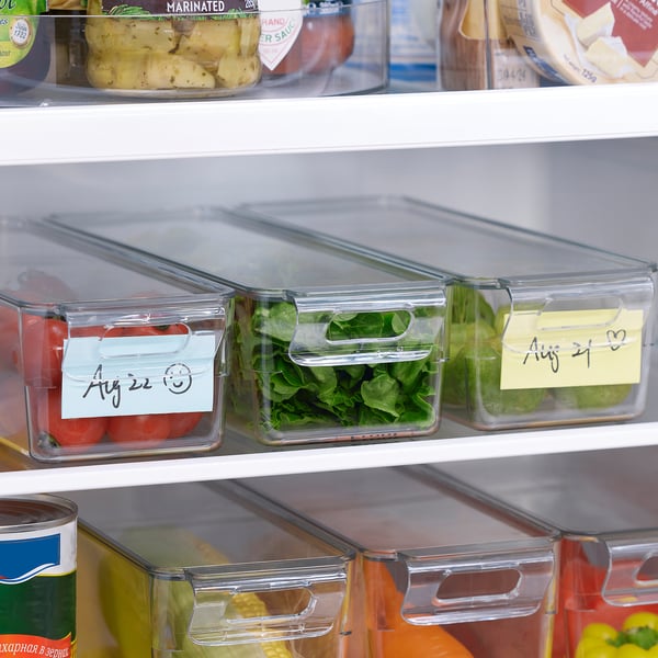 Clear fridge storage boxes with lids, labels, and handles, organising vegetables and fruits in a well-structured fridge.