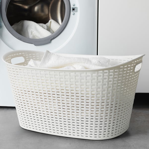 White laundry basket with handles in front of dryer, overflowing with white clothes.