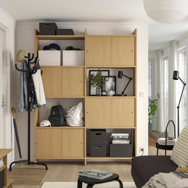 Wooden storage unit with open shelves and closed cabinets. Holds various items like bags and boxes. Standing near a black coat rack.