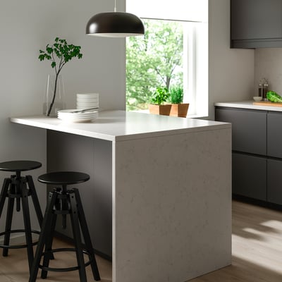 Modern kitchen with white island, black stools, dark cabinets, and greenery view.