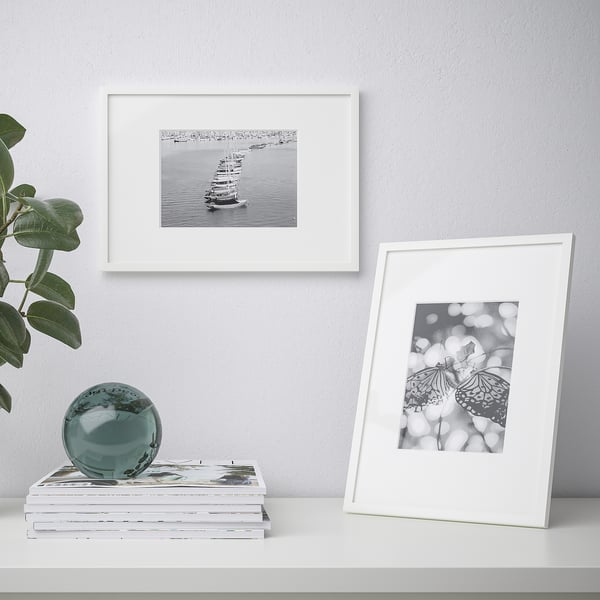 Display shelf with a butterfly photo frame, boat photo, stack of books, and glass orb. The frame holds an upright black and white picture.