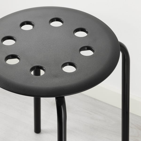 Black modern stool with round seat and metal legs, designed for stacking, shown on light-colored floor.