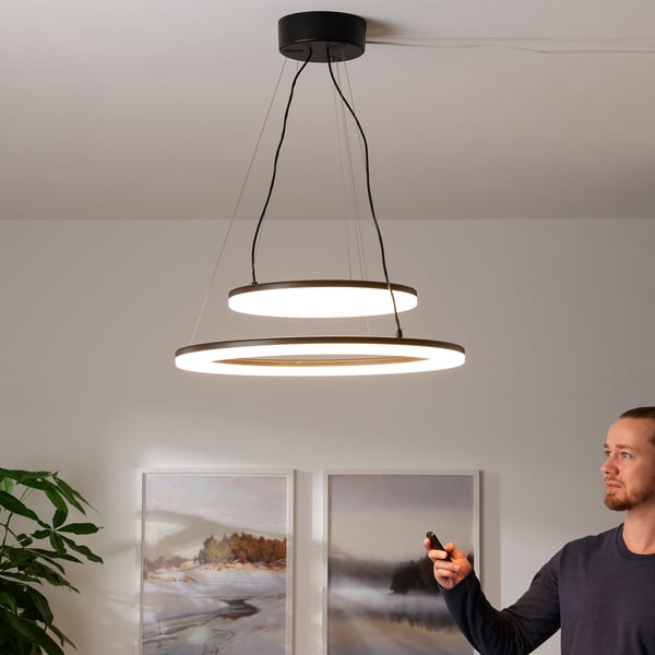 Person adjusts modern pendant light with remote.