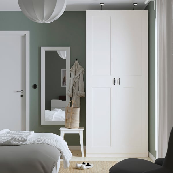 Modern bedroom with white PAX wardrobe, sage walls, black handles, bench, and mirror.