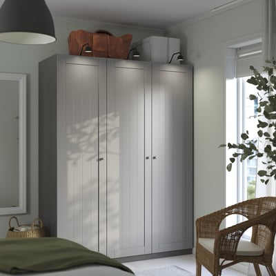 Grey PAX wardrobe, tall with clean lines, multiple panels. Topped with bags and a box, beside a lamp and mirror.