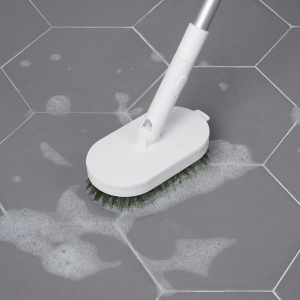 White brush with a long handle, cleaning a gray-tiled floor with soap suds; part of PEPPRIG cleaning system.