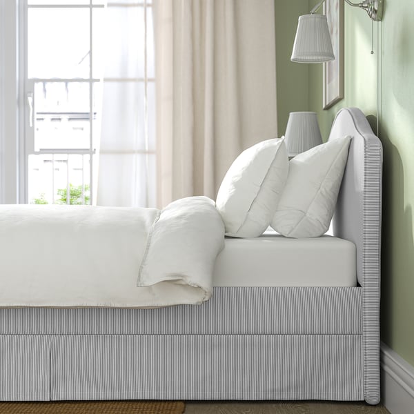 Cosy bed with curved headboard, plush pillows, and clean linens. Bright, airy room with large windows and light green walls.