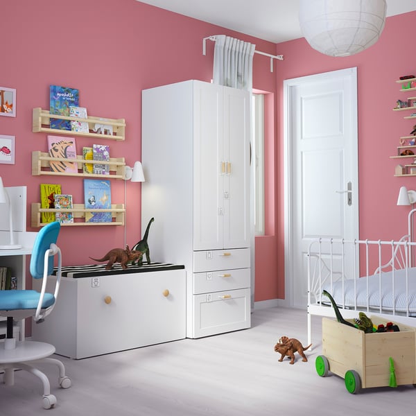 Kids room with pink walls, white furniture: wardrobe, desk, bed, dinosaur toys, bookshelves.