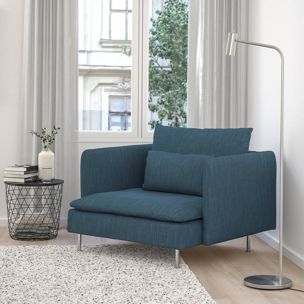 Blue upholstered armchair near a window, with a floor lamp and side table.