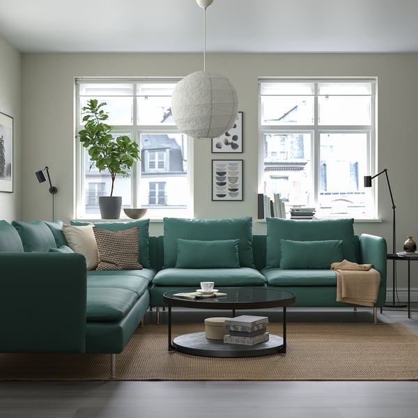 Modern living room featuring SÖDERHAMN green l-shaped sofa, glass coffee table, large windows, plant, and unique lamp.