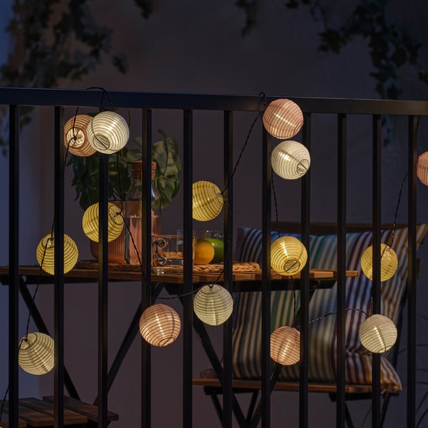 Balcony at night with string lights, cushioned chairs, and plants.