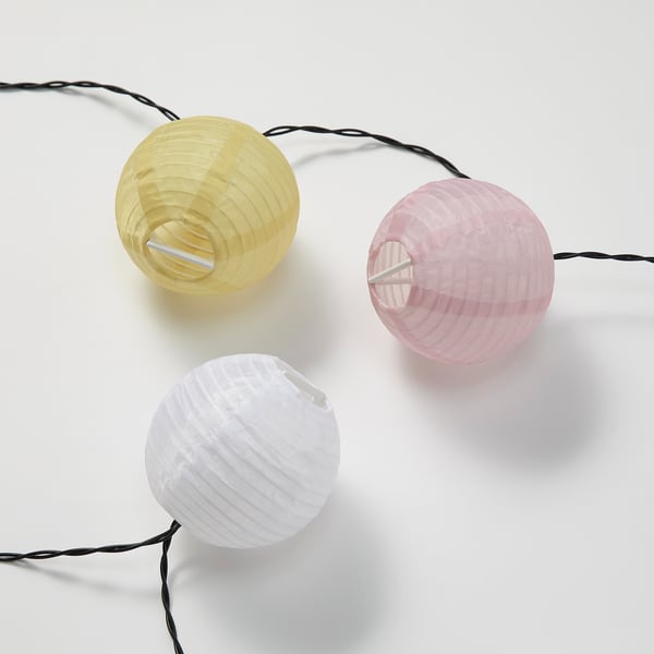 Three colourful lanterns - yellow, white, pink - hang, casting soft glow. Outdoor decor.