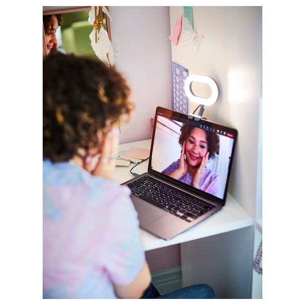 Person with curly hair on video call, smiling at laptop with ring light attached.