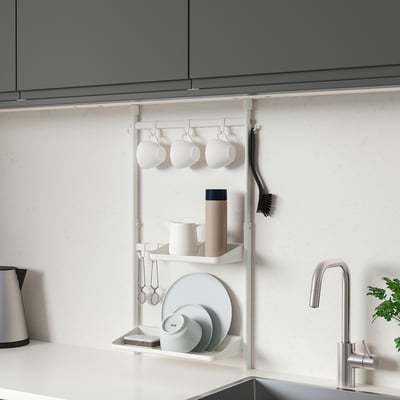 Modern white SUNNERSTA kitchen rack holding cups, plates, and mugs under grey cabinet.