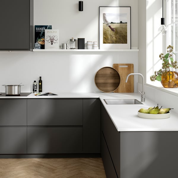 Modern kitchen with grey TÄRNHULT glass walls, white counter, steel sink, decor, and hanging light.