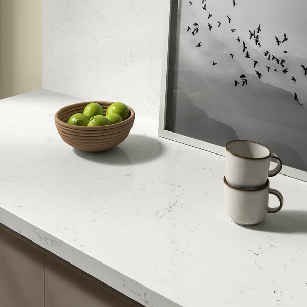 A kitchen counter with a bowl of limes and cups, featuring a white, stain-resistant wall panel made from recycled glass.
