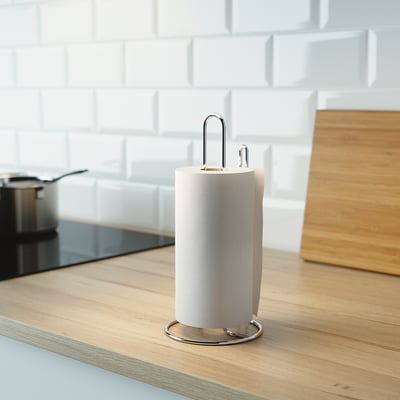 Kitchen counter with light wood surface; stainless steel paper towel holder stands centre, roll positioned for easy tear.