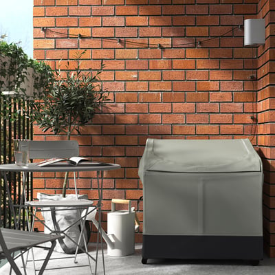 Grey outdoor storage box with vents and handles next to chairs and plant.