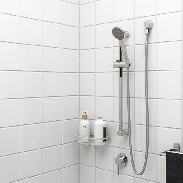 Shower area with VALLAMOSSE silver rail, handheld shower, glass shelf holding two white bottles.