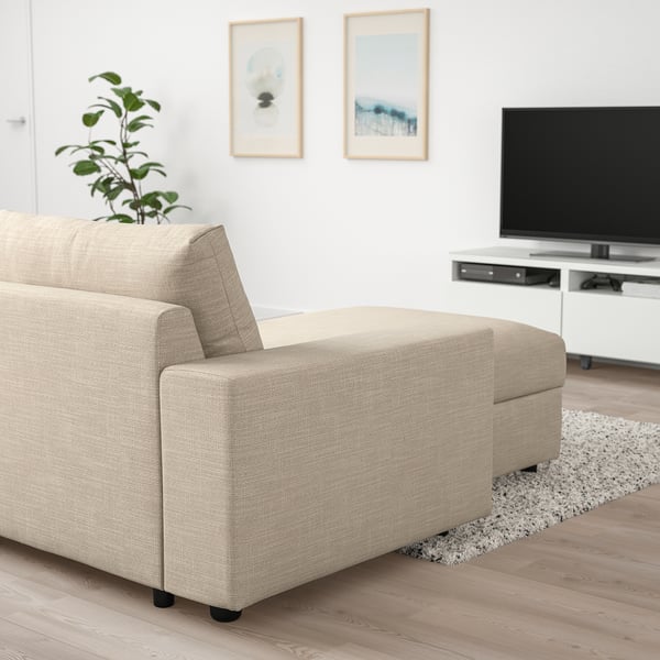 Minimalist living room with beige sectional sofa, tv, wooden floors, and plant.