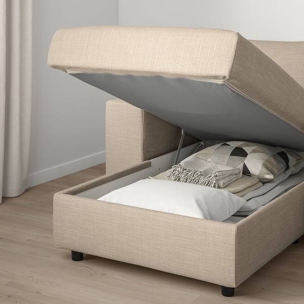 Modern beige sofa with open storage compartment showing bedding and pillows. Lid prevents closing.