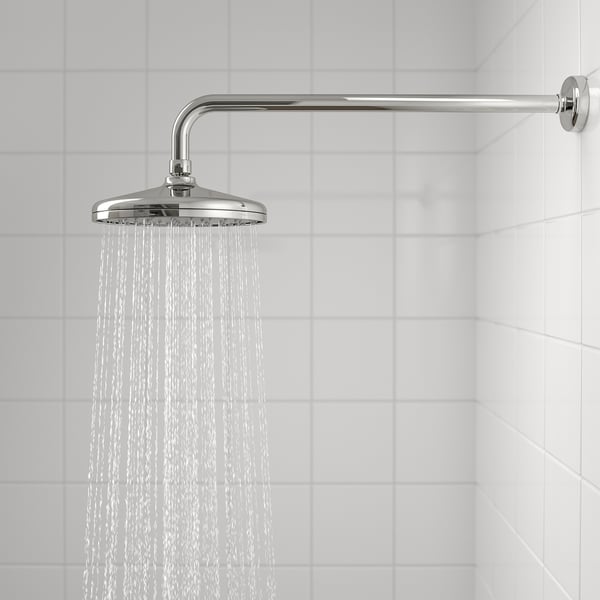 Showerhead with full spray function, emitting a wide, even flow for a rainfall feel. Chrome finish, mounted on white tiled wall.