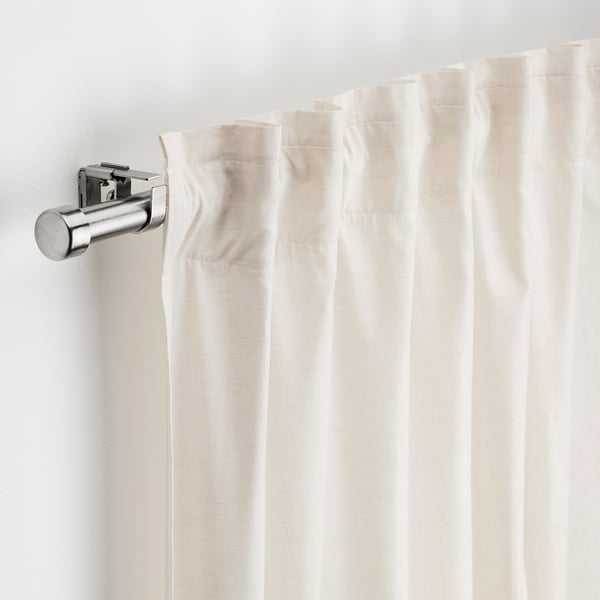 Window curtain rod with brackets and finials, holding creamy curtains.